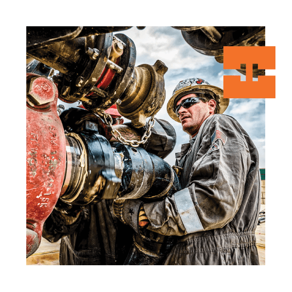 Worker in protective gear examining industrial machinery outdoors.
